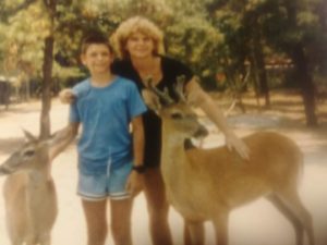 Young Gregory wuith his mom standing next to 2 deer.