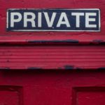 A mail slot on a red door that has a private sign above it