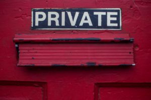 A mail slot on a red door that has a private sign above it